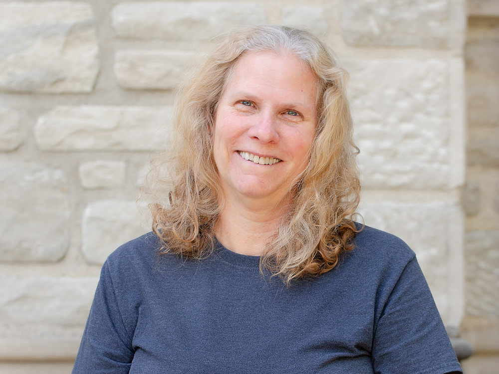 A woman with long, curly blonde hair wearing a grey tee-shirt.