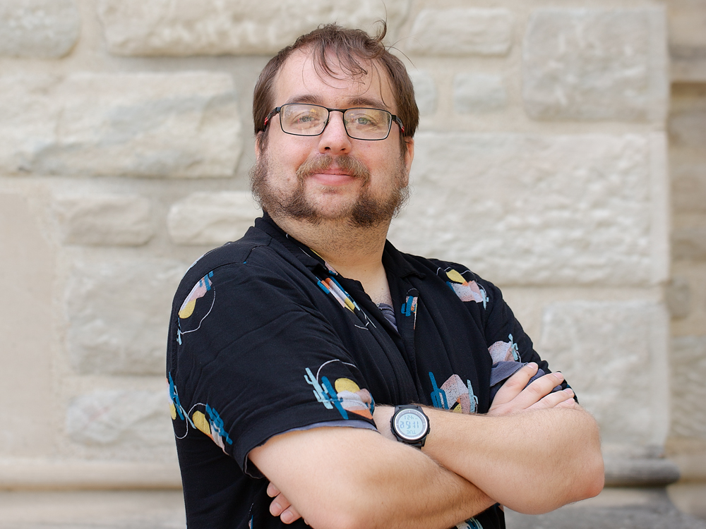 A man with glasses and a black short sleeve shirt.