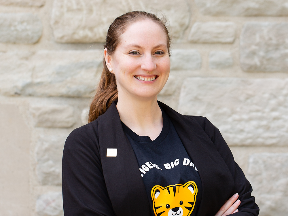 A woman with her hair pulled back wearing a black shirt with a tiger cub and a black blazer.