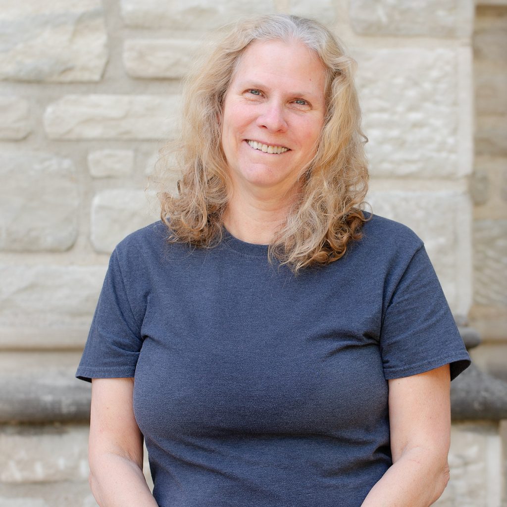 A woman with long, curly blonde hair wearing a grey tee-shirt.