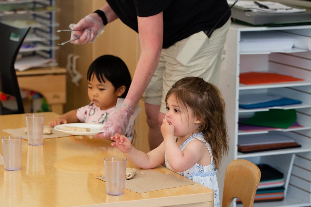 An early childhood professional helps two young children with lunch as they sit a communal table at the Child Development Lab.