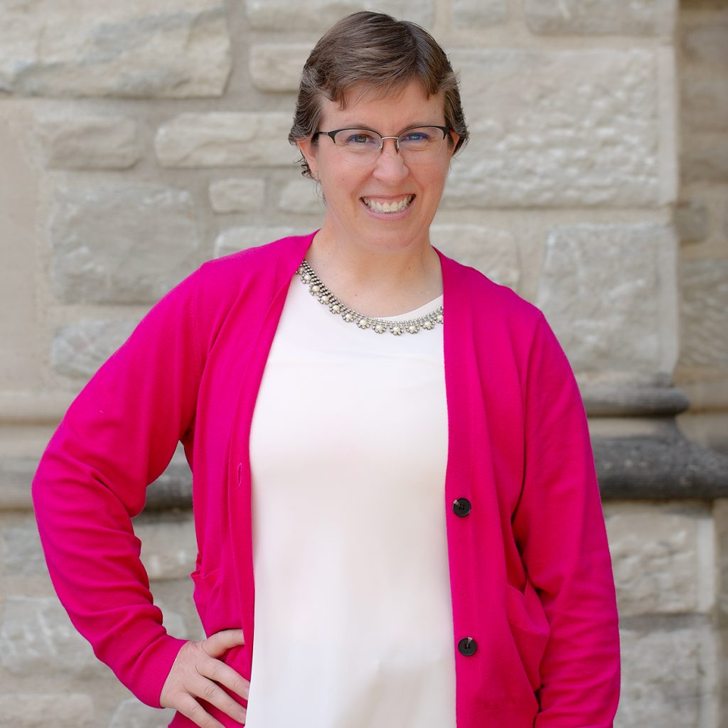 A woman with short brown hair wearing a white shirt and a pink sweater.