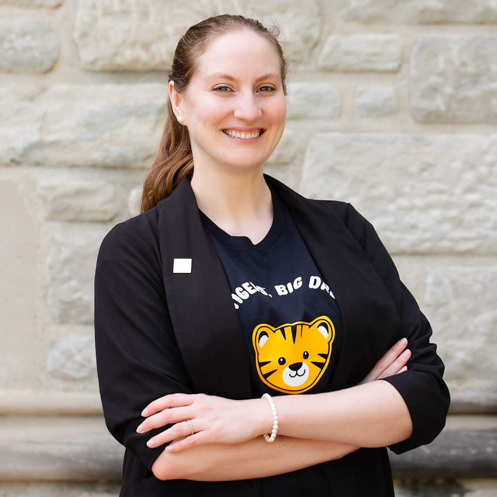 A woman with her hair pulled back wearing a black shirt with a tiger cub and a black blazer.