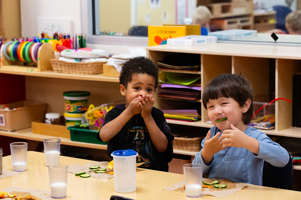 Two young boys eat lunch at a communal table.