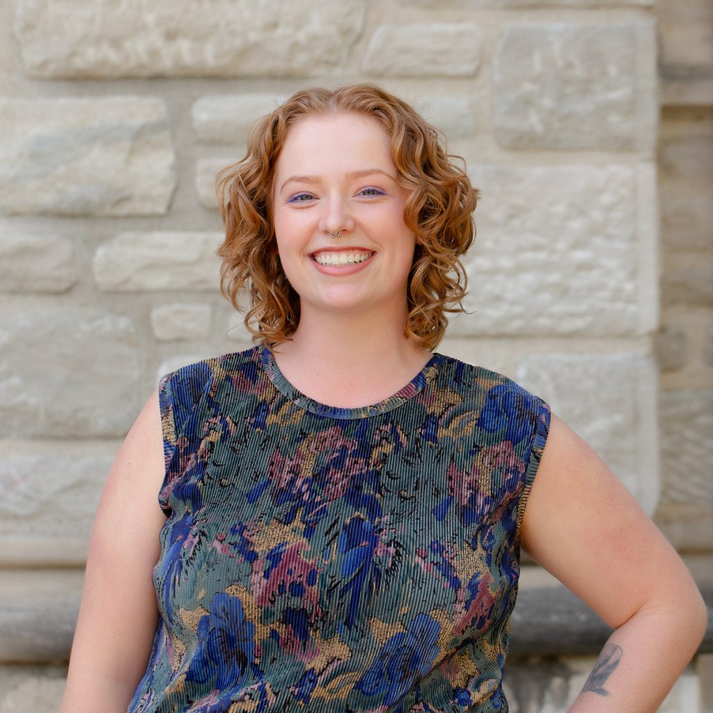 A woman with short red hair wearing a multicolored blue shirt.