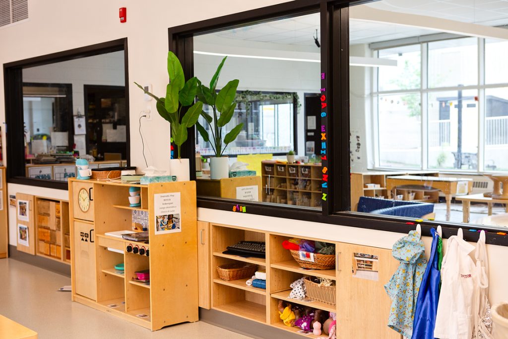 An early childhood classroom play area with dress-up clothes and mirrored observation area.