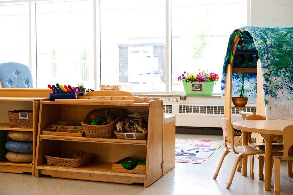 An early childhood classroom with a play area, tent, flowers in the window, and a table and chairs.