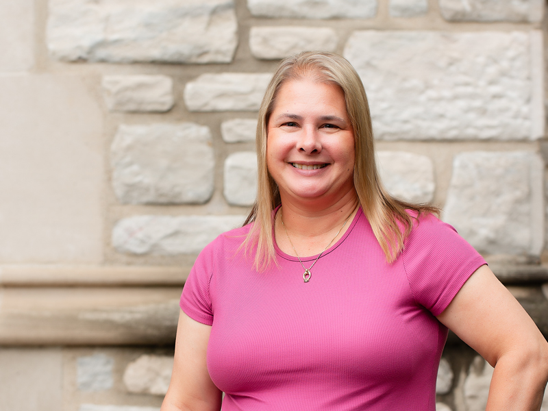 A woman with short blonde hair wearing a pink teeshirt.