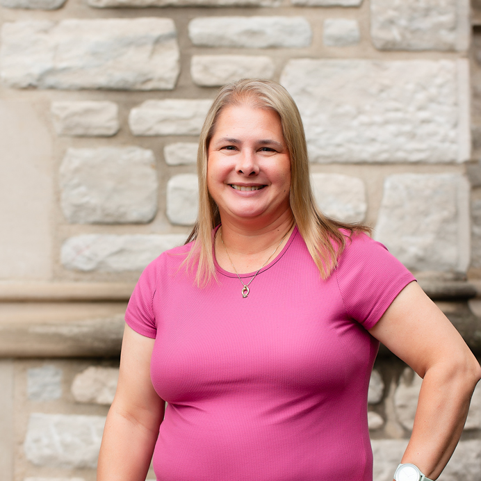A woman with short blonde hair wearing a pink teeshirt.