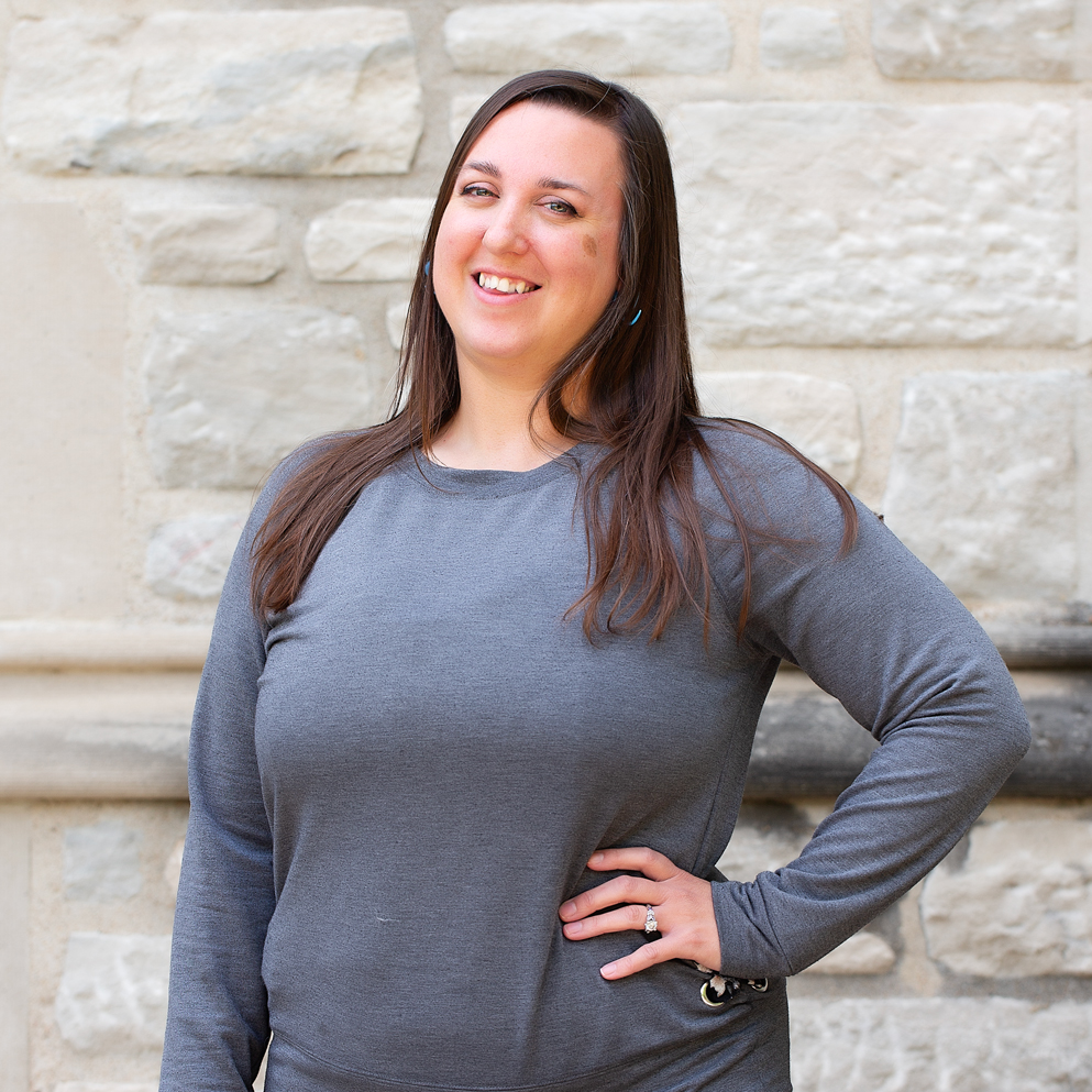 A woman with long brown hair wearing a grey shirt.