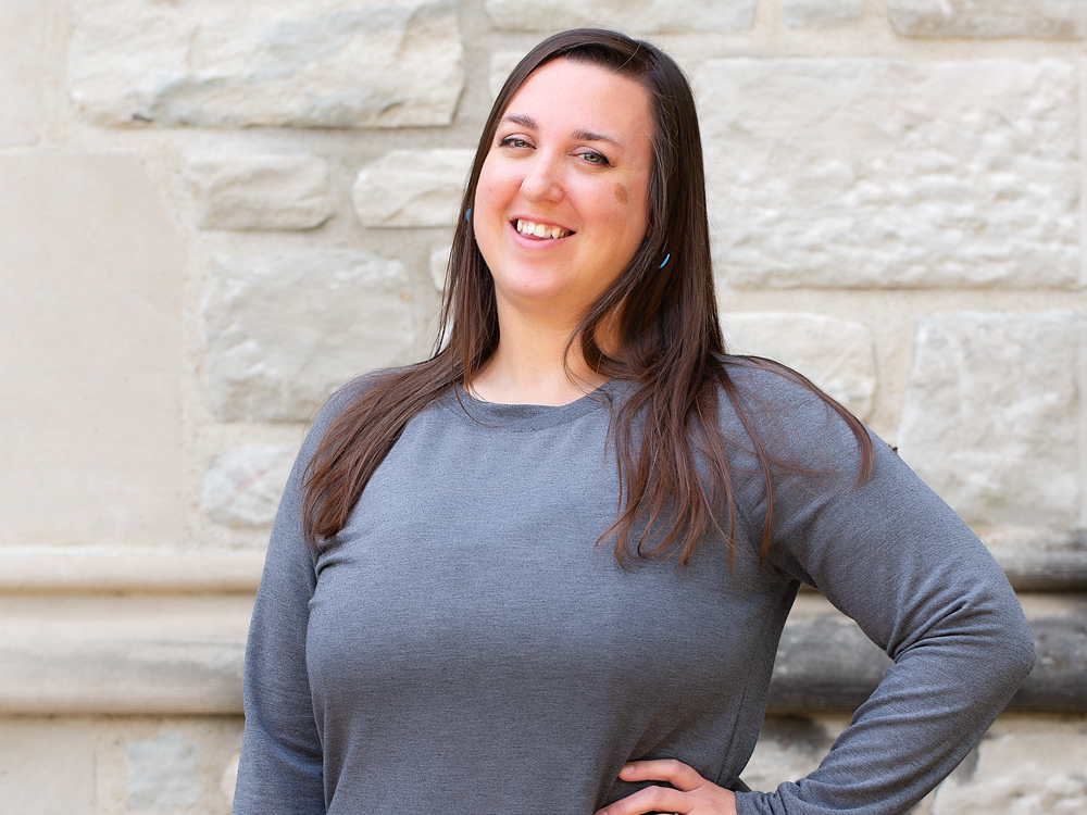 A woman with long brown hair wearing a grey shirt.